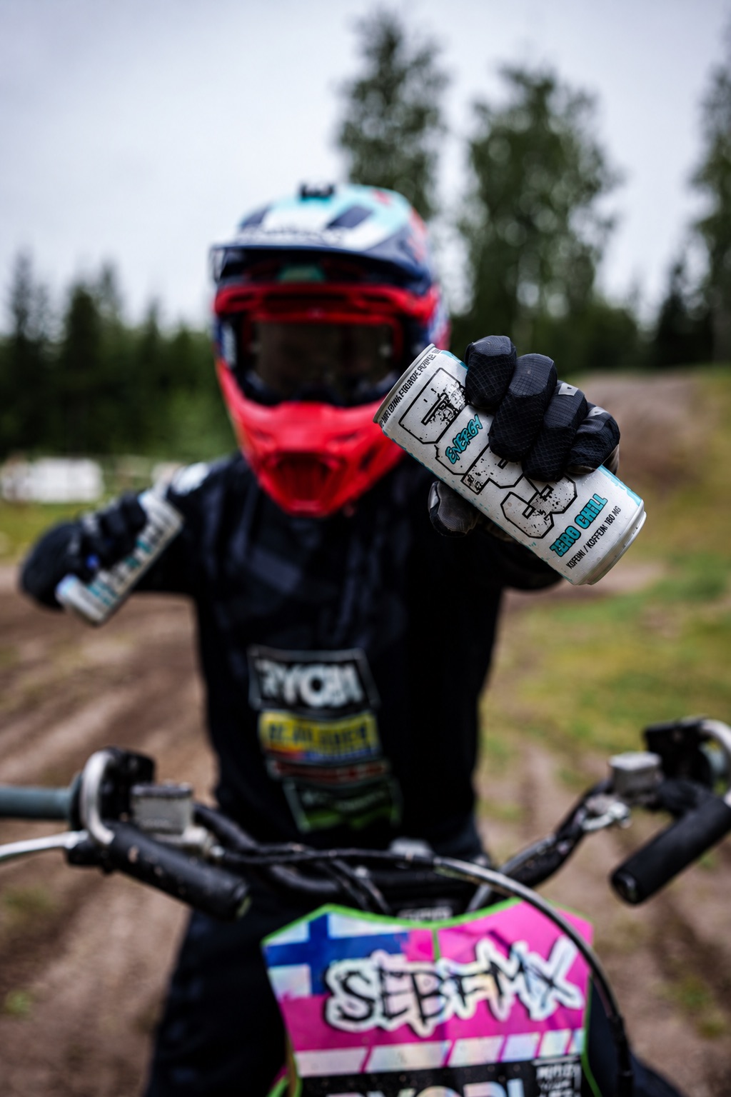 Motocross rider holding a DOP3 Energy can in front of the camera while sitting on a dirt bike